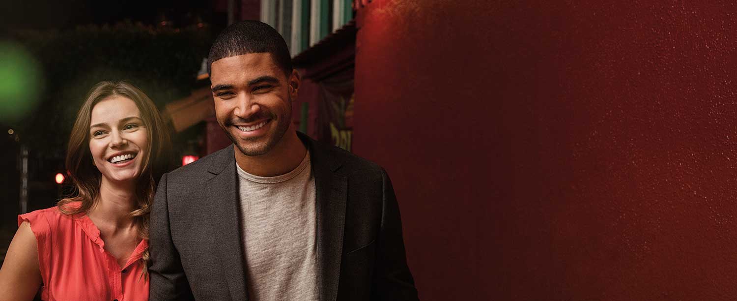 A man and woman smiling together at night, illuminated by soft lights in a warm and joyful atmosphere.