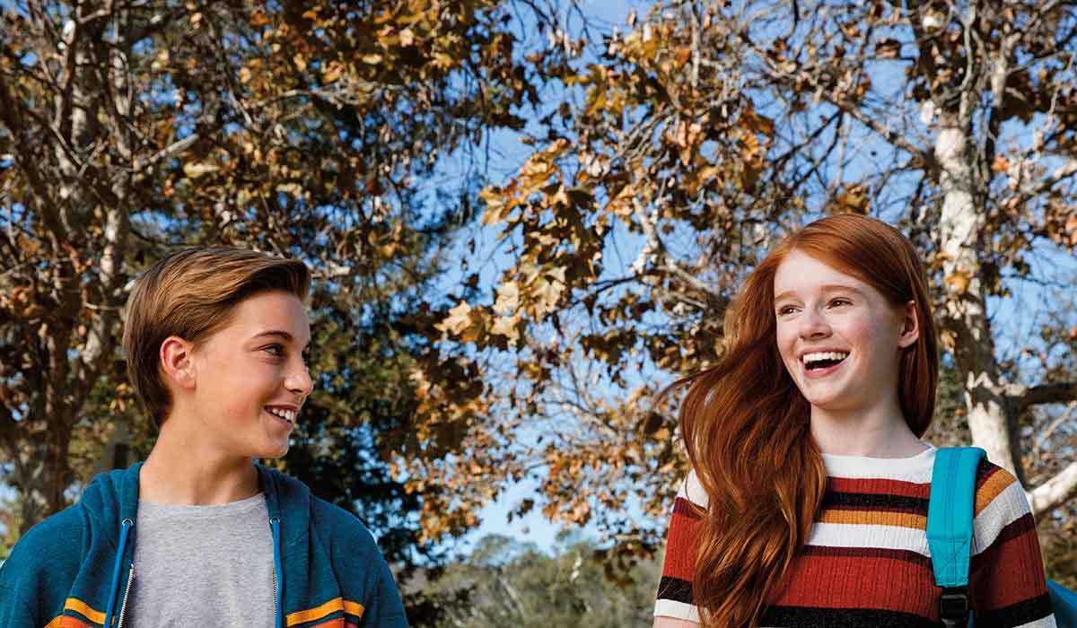 Two young people are smiling and laughing together in a sunny park, enjoying their time outdoors.