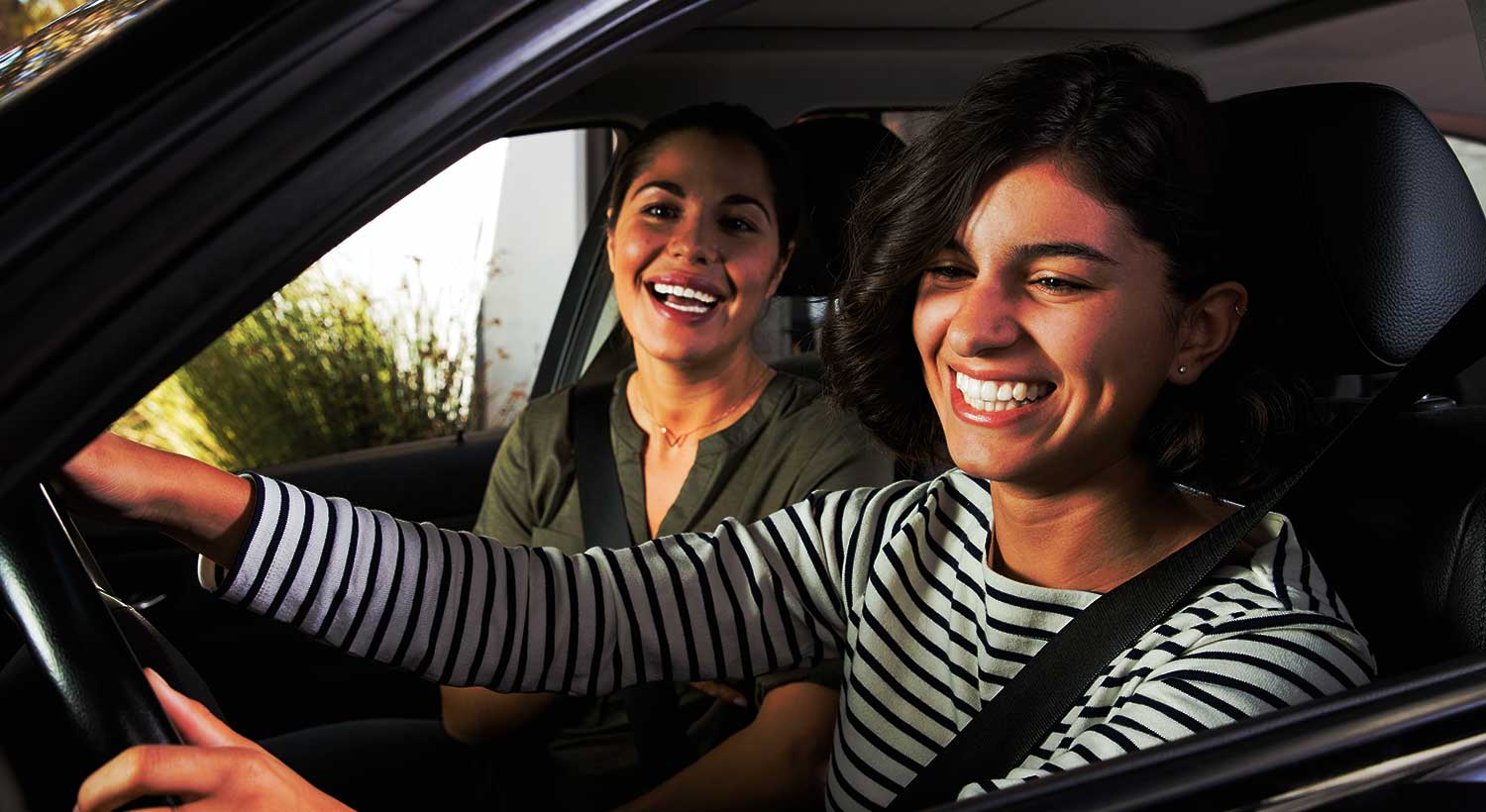 Two women sitting in car's front seats, smiling happily.